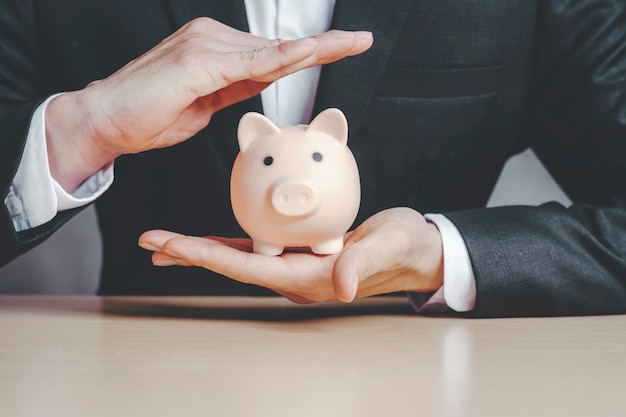 Business man wearing a black suit and insurance to protect the piggy bank in the hand Concepts of life insurance.