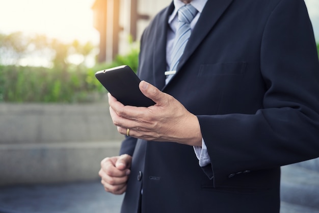 business man wearing black suit and using modern smartphone in outdoor