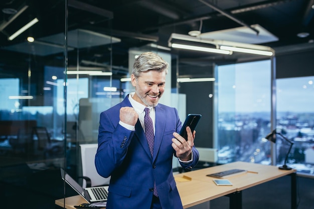 Business manager businessman in a modern office uses the phone happy and happy experienced man