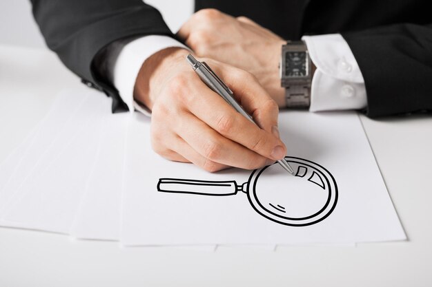 business, marketing, planning and people concept - close up of male hands with pen drawing lens on white paper