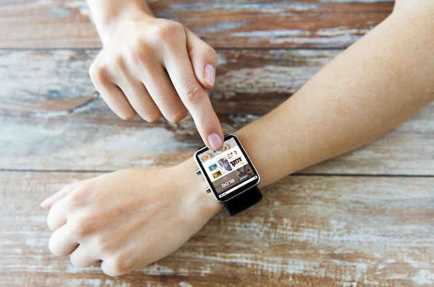 business, modern technology, blogging, media and people concept - close up of female hands setting smart watch with internet blog on screen on wooden table