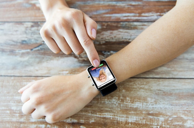 business, modern technology, communication and people concept - close up of female hands setting smart watch with incoming call on screen on wooden table