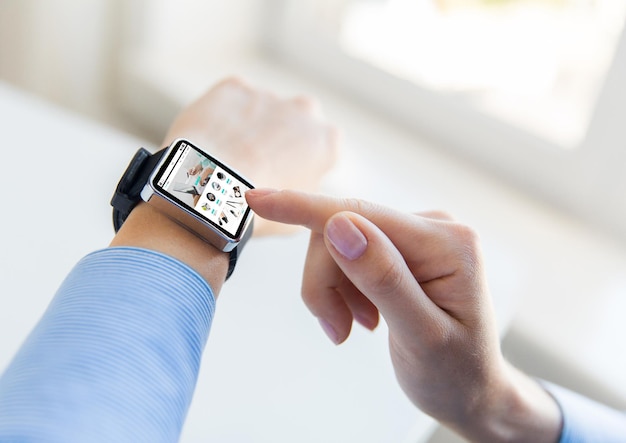 business, modern technology, internet shopping and people concept - close up of female hands setting smart watch with online shop on screen at office