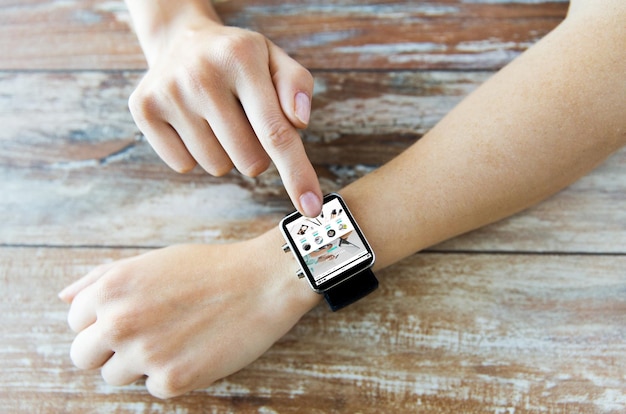 business, modern technology, internet shopping and people concept - close up of female hands setting smart watch with online shop on screen on wooden table