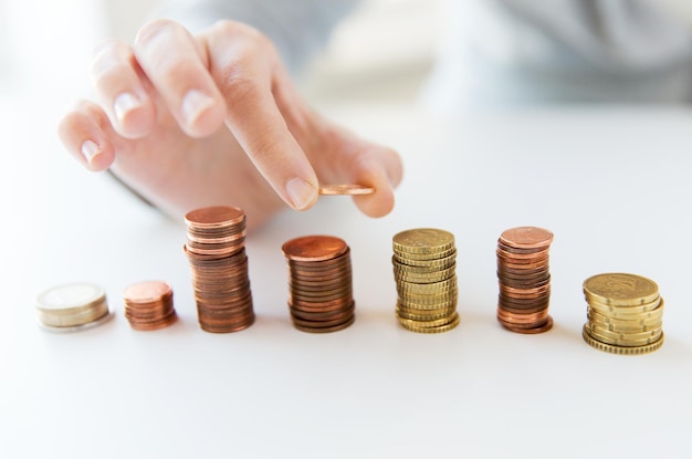 business and money saving concept - close up of female hand putting euro coins into columns in office