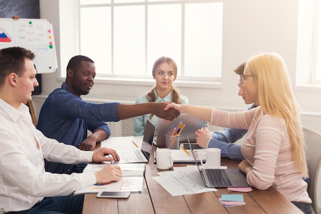 Business multiethnic handshake at office corporate meeting, contract conclusion and successful agreement concept. Cheerful businessman and businesswoman hands meet, copy space