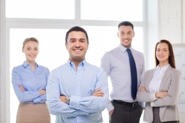 business and office concept - smiling handsome businessman with crossed hands and team in office