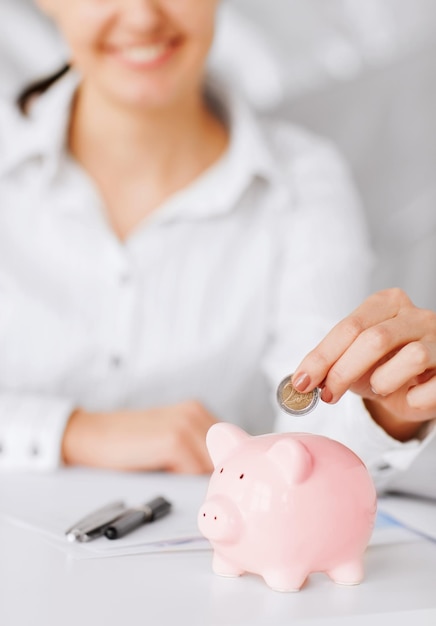 business, office, household, school, tax and education concept - woman hand putting coin into small piggy bank