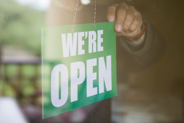 Business owner hanging an open sign at a glass door. We are open.