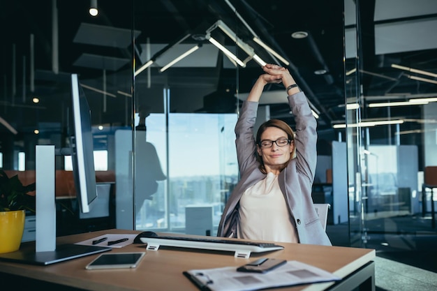 Business owner woman resting during working hours puts her hands behind her head thinks about business plans works in a modern office