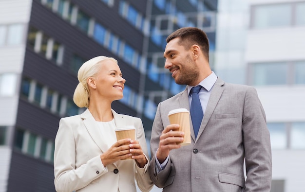 business, partnership, hot drinks and people concept - smiling businessmen with paper cups standing over office building