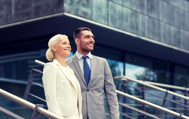 business, partnership, success and people concept - smiling businessman and businesswoman standing over office building