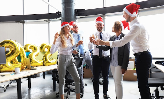 Business people are celebrating holiday in modern office drinking champagne and having fun in coworking. Merry Christmas and Happy New Year 2022.