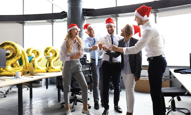 Business people are celebrating holiday in modern office drinking champagne and having fun in coworking. Merry Christmas and Happy New Year 2022.