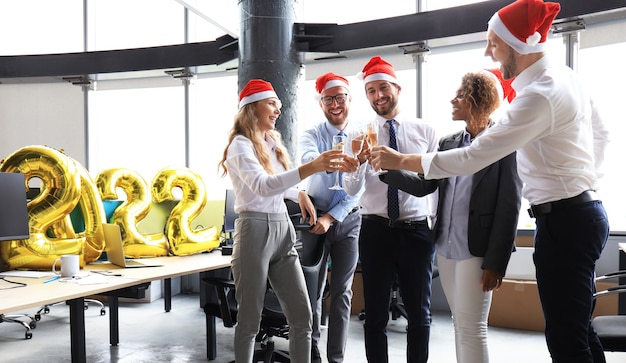 Business people are celebrating holiday in modern office drinking champagne and having fun in coworking. Merry Christmas and Happy New Year 2022.