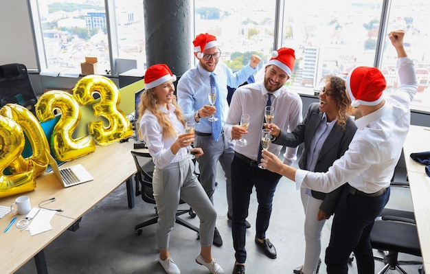 Business people are celebrating holiday in modern office drinking champagne and having fun in coworking Merry Christmas and Happy New Year 2023