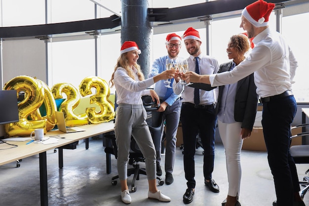 Business people are celebrating holiday in modern office drinking champagne and having fun in coworking Merry Christmas and Happy New Year 2023