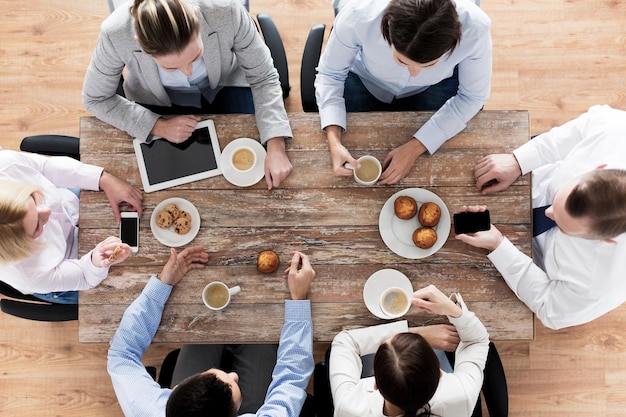 business, people, break and team work concept - close up of creative team meeting and drinking coffee with muffins during lunch in office