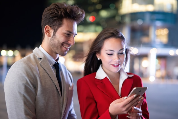 Business people businessman and businesswoman using a smartphone at night in a city