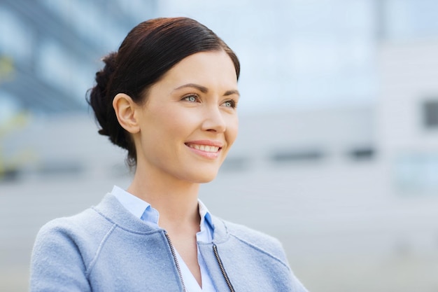 business and people concept - young smiling businesswoman over office building