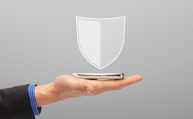 Photo business, people and cyber protection concept - close up of male hand with virtual antivirus program shield icon above smartphone over gray background