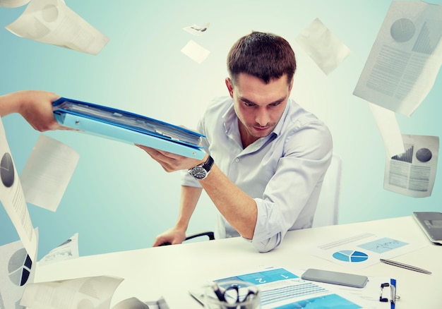 business, people, deadline and paperwork concept - businessman taking folder from secretary over blue background and falling papers