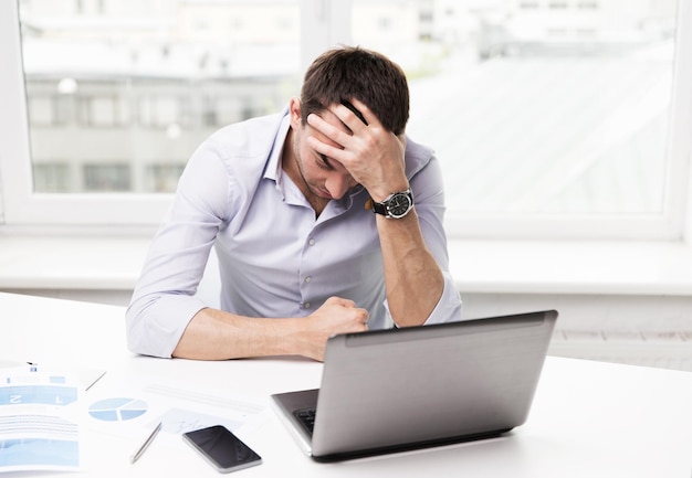 business, people, fail, paperwork and technology concept - businessman with laptop computer and papers working in office