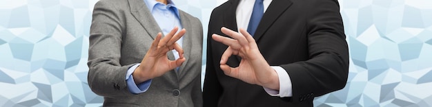 business, people, gesture and cooperation concept - close up of businessman and businesswoman showing ok sign over blue low poly graphic background