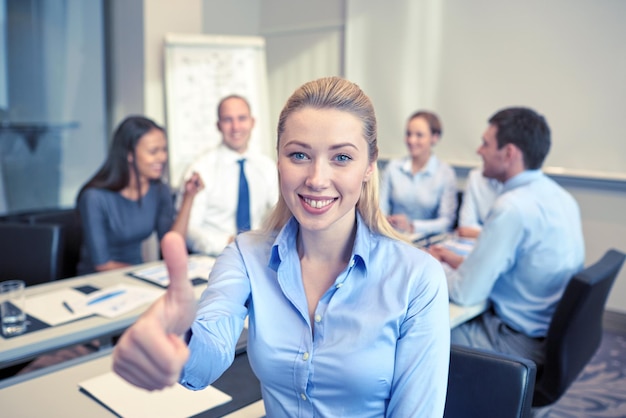 business, people, gesture and teamwork concept - smiling businesswoman showing thumbs up with group of businesspeople meeting in office