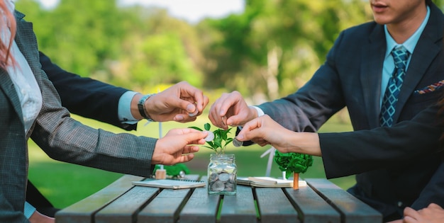 Photo business people put coin to money saving glass jar on outdoor table as sustainable money growth investment or ecosubsidize green corporate promot and invest in environmental awareness gyre