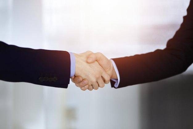 Business people shaking hands, close-up. Group of unknown businessmen standing in a sunny modern office. Teamwork, partnership and handshake concept.