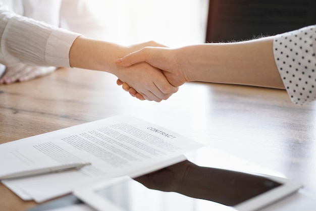 Business people shaking hands above contract papers just signed on the wooden table, close up. Lawyers at meeting. Teamwork, partnership, success concept