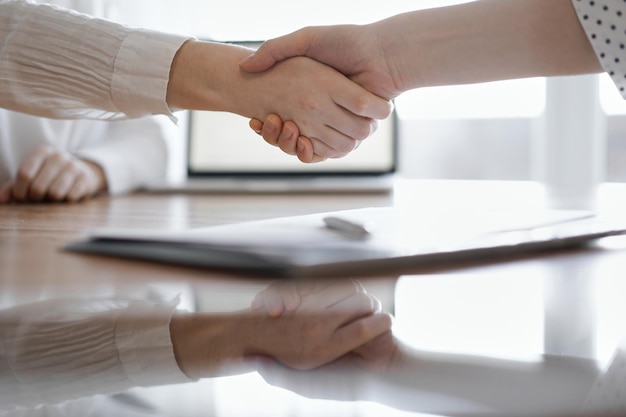 Business people shaking hands above contract papers just signed on the wooden table, close up. Lawyers at meeting. Teamwork, partnership, success concept.