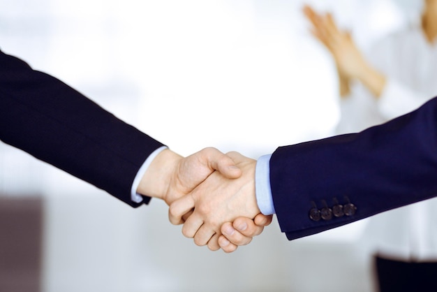 Business people shaking hands at meeting or negotiation, close-up. Group of unknown businessmen and a woman standing in a modern office. Teamwork, partnership and handshake concept.