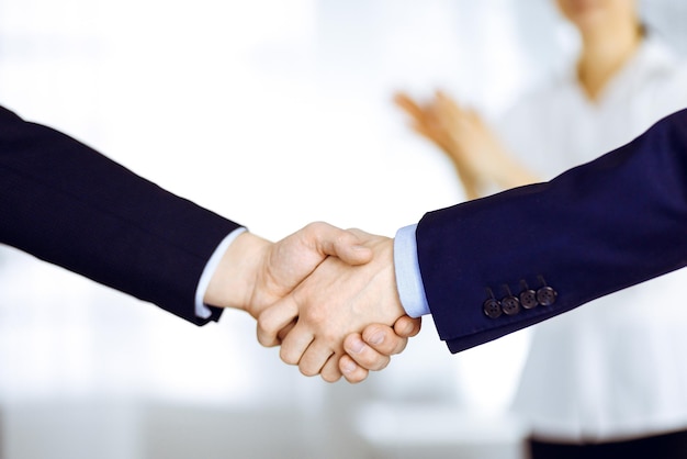 Business people shaking hands at meeting or negotiation, close-up. Group of unknown businessmen and a woman standing in a modern office. Teamwork, partnership and handshake concept.