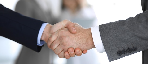 Business people shaking hands while standing with colleagues after meeting or negotiation, close-up. Group of unknown businessmen and women in modern office. Teamwork, partnership and handshake concep