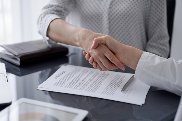 Business people signing contract papers while sitting at the glass table in office, closeup. Partners or lawyers working together at meeting. Teamwork, partnership, success concept.