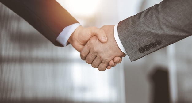 Business people standing and shaking hands in sunny office, close-up. Handshake and marketing.