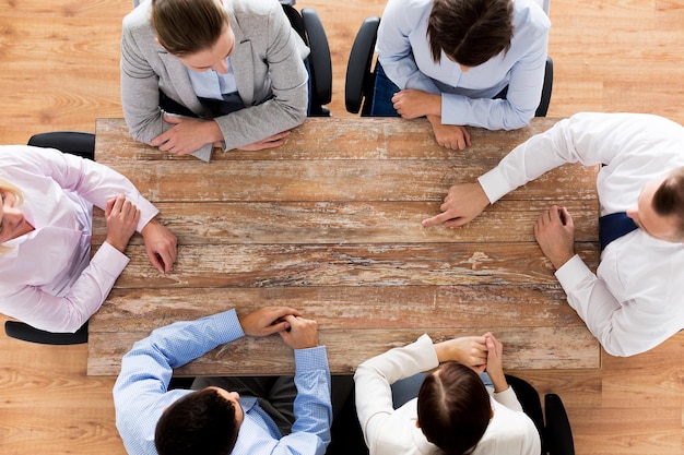 business, people and team work concept - close up of creative team sitting at table and pointing finger to something in office