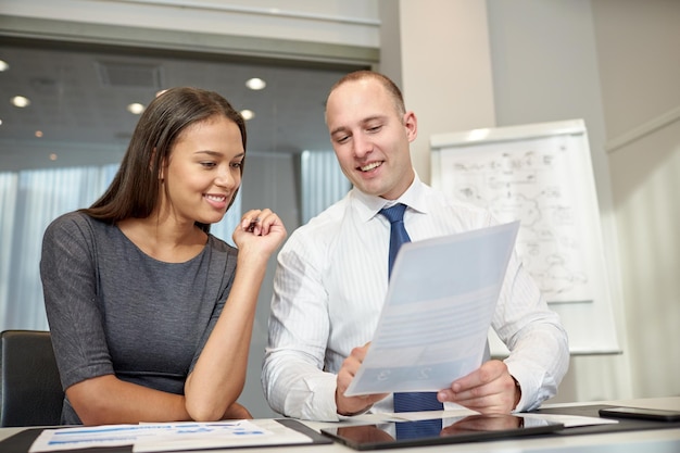 business, people and teamwork concept - smiling businessman and businesswoman with papers meeting in office