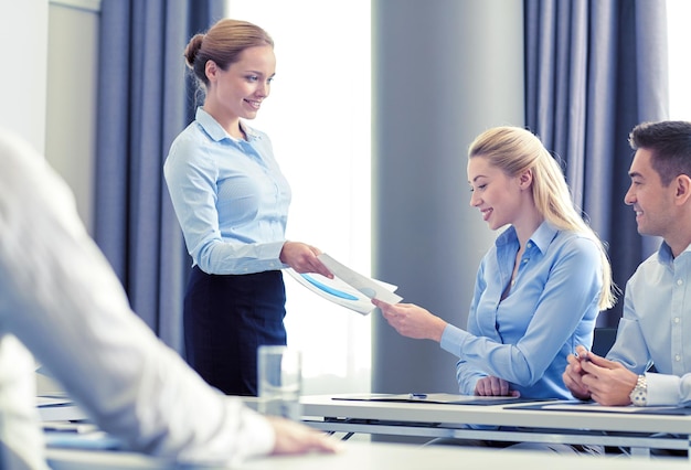 business, people and teamwork concept - smiling woman giving papers to group of businessmen in office