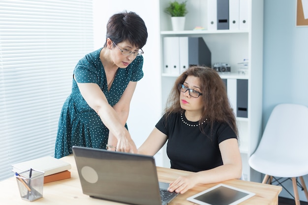 Business people, technology and communication concept - Mid-aged lady helping her female colleague