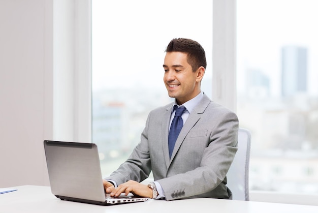 business, people and technology concept - happy smiling businessman in suit working with laptop computer in office