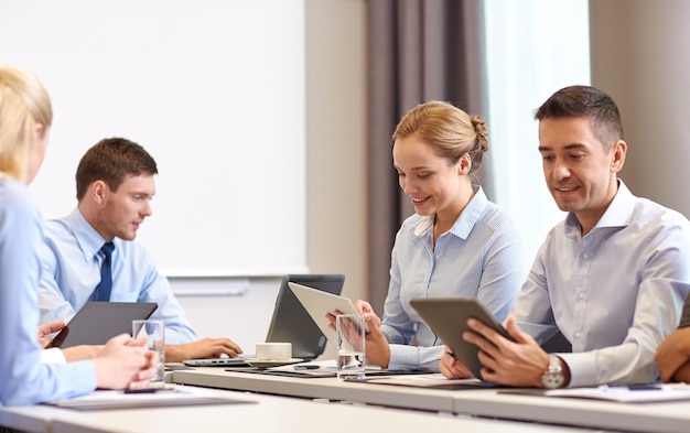 business, people and technology concept - smiling business team with tablet pc computer meeting in office