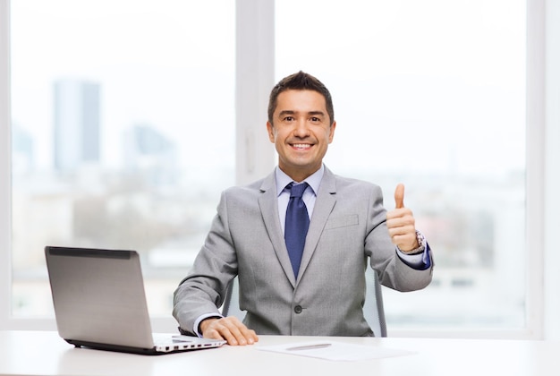 business, people and technology concept - smiling businessman in suit working with laptop computer in office