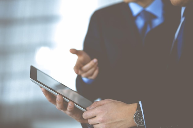 Business people use a tablet computer for discussion of their new project, standing in a modern office. Unknown businessman or male entrepreneur with a colleague at workplace. Teamwork and partnership