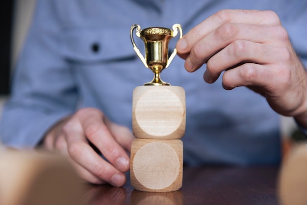 Business person arranging large wooden blocks with a winning trophy Business success