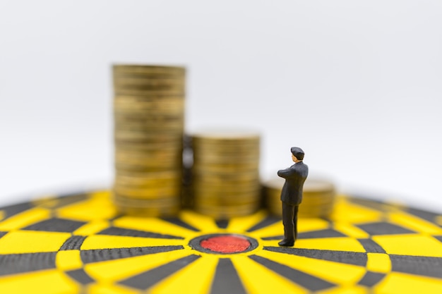 Photo business planning,  money, target and goal cover concept. businessman miniature figure people standing and looking to stack of gold coins on yellow and black dartboard.