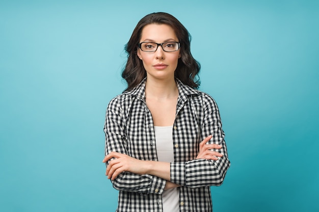 Business portrait of a young woman a charming brunette with glasses looks at the camera crossing her