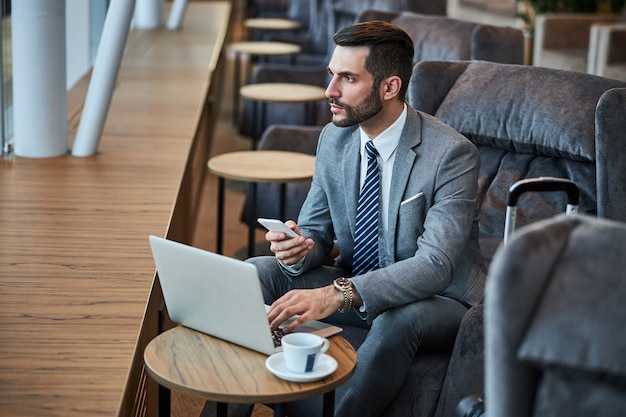 Business professional taking a smartphone while using a laptop